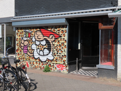 912764 Afbeelding van een Utrechtse kabouter (KBTR) die een shaslick (?) eet, op een rolluik voor de leegstaande winkel ...